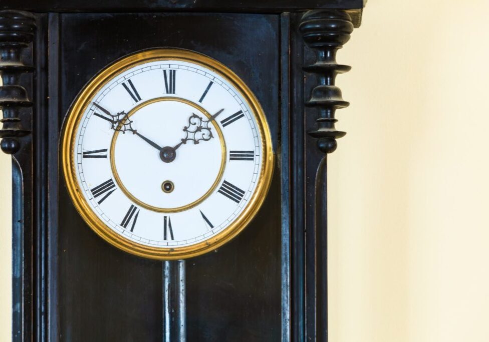 Closeup old big wooden pendulum clock hanging on wall